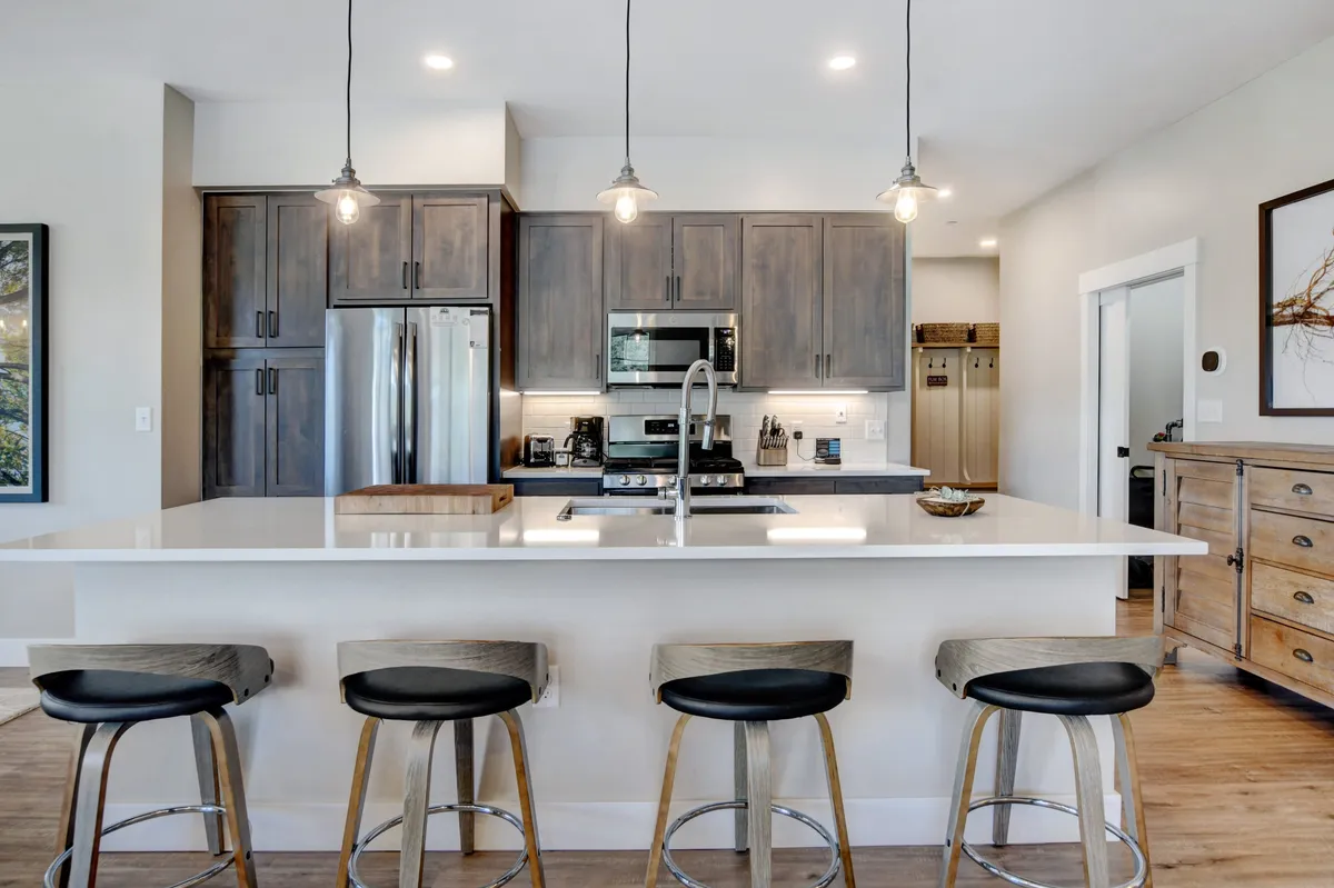 This image focuses on a contemporary kitchen featuring an expansive island countertop, matching stools, modern cabinetry, and built-in premium appliances. Natural light floods the space, highlighting the kitchen's functionality and inviting ambiance, perfect for both meal prep and socializing.