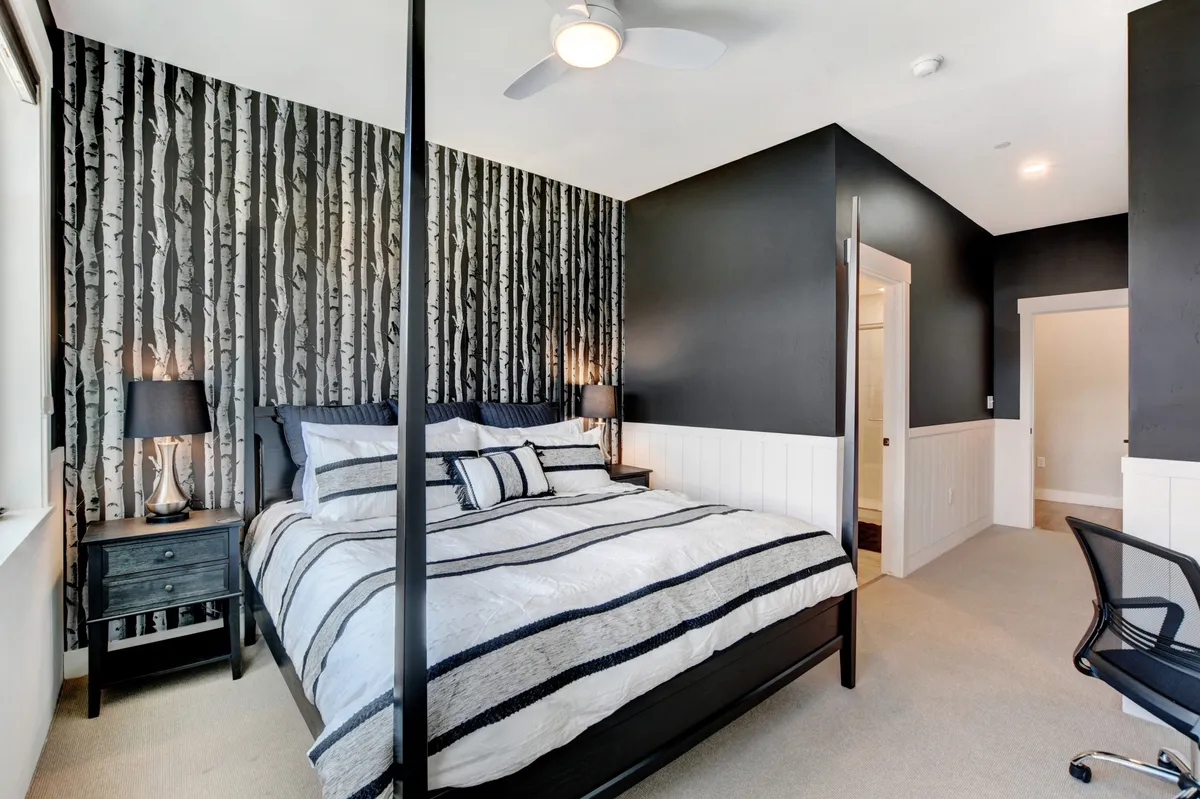 A cozy, modern bedroom featuring a four-poster bed with striped bedding, birch tree wallpaper, and nightstands with lamps. Soft morning light filters through the window, creating an ideal space for restful sleep and relaxation.