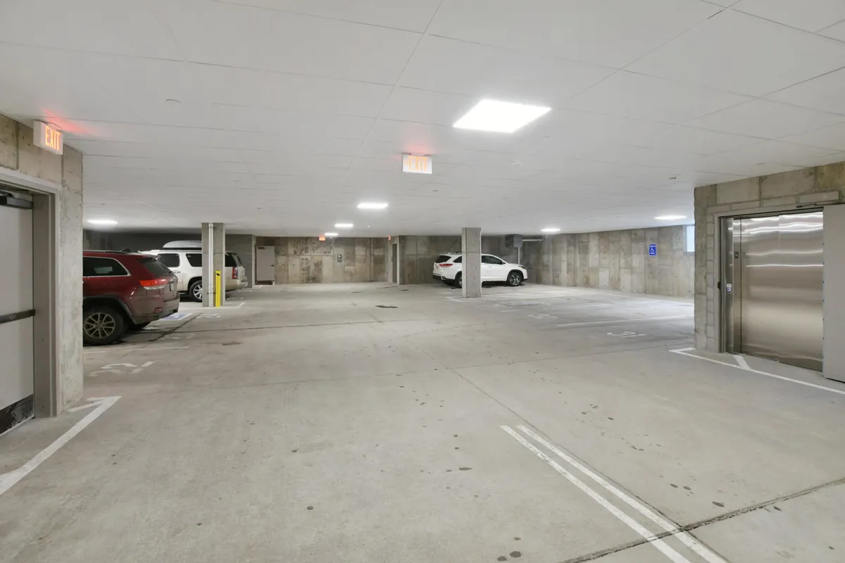 The interior of an assigned heated garage with vehicles parked in designated spaces, sturdy concrete pillars, and bright overhead lighting. The environment feels secure, functional, and easily accessible.