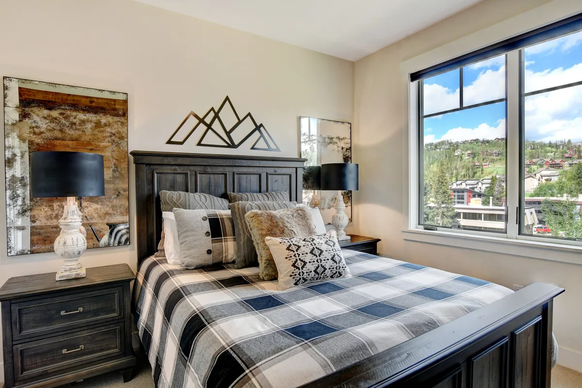 A comfortable bedroom with plaid bedding, mountain-themed wall décor, and black-shaded lamps. Large mirrors reflect beautiful mountain views, reinforcing a peaceful and inviting setting.